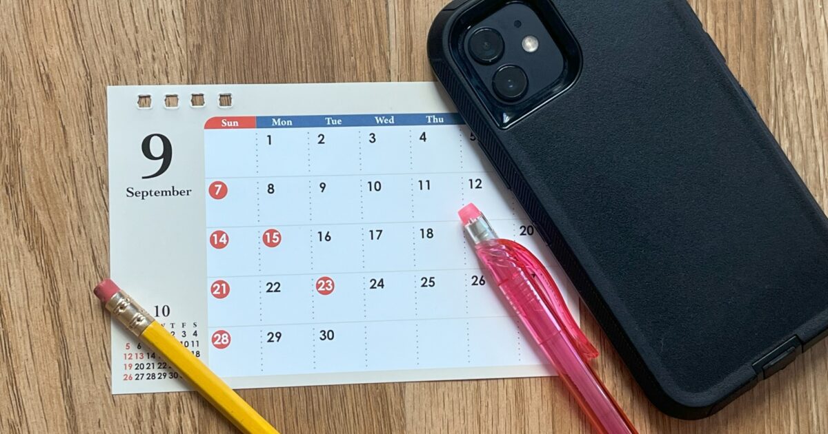 9月のカレンダーとスマートフォンと鉛筆と赤いボールペンの平置き構図