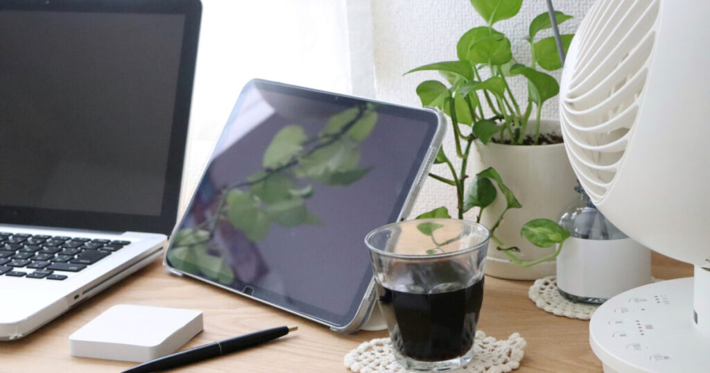 ノートパソコンとタブレットと観葉植物と黒い飲み物の作業スペース