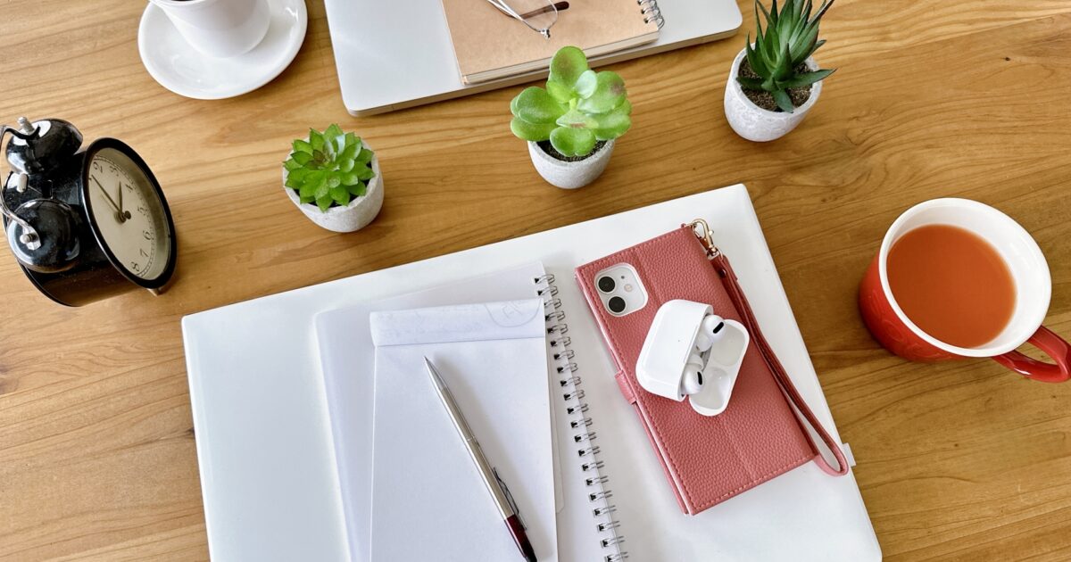 観葉植物とノートとスマートフォンとコーヒーが並ぶ木製デスク