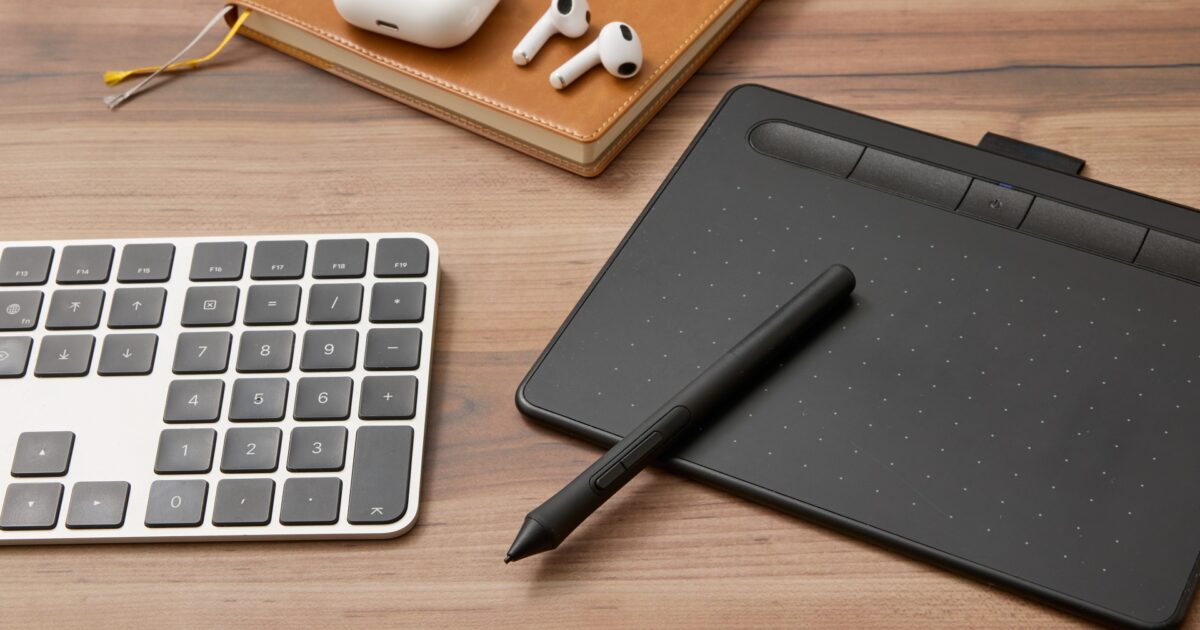 ペンタブレットとワイヤレスイヤホンとキーボードとノートのデスクトップ