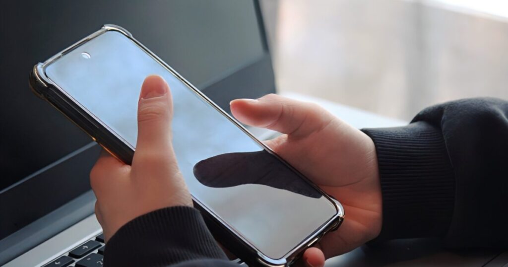 ノートパソコンの前でスマートフォンを操作する手元