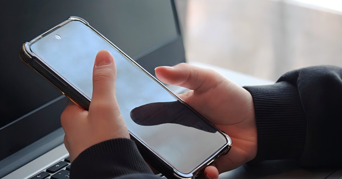 ノートパソコンの前でスマートフォンを操作する手元